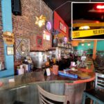 Área de bar em restaurante com paredes de tijolos, decoração colorida e vários bancos de bar.