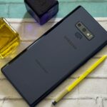 Comparação da parte traseira do Galaxy S25 e S26, destacando a lente da câmera, sobreposta com ícones de polegar para baixo.