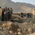 Moradores locais e trabalhadores da defesa civil observam enquanto uma escavadeira limpa os escombros de uma casa atingida por um ataque transfronteiriço do exército paquistanês no distrito de Behsud, na província de Nangarhar, no Afeganistão, em 22 de fevereiro.