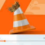 Mascote Android verde espiando por trás de um grande cone de trânsito VLC laranja em um fundo estampado.
