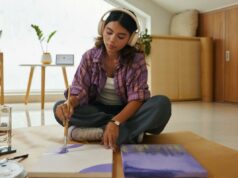 O autismo provavelmente afeta meninas tanto quanto meninos: “Pode não ser mais distinguível” Uma jovem com fones de ouvido sentada no chão, pintando em uma tela com tinta roxa.