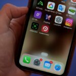 Close de uma mão segurando um smartphone exibindo aplicativos, incluindo