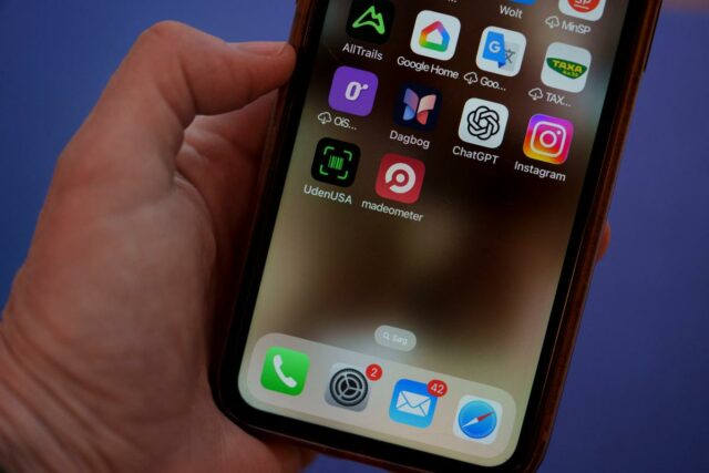 Close de uma mão segurando um smartphone exibindo aplicativos, incluindo 