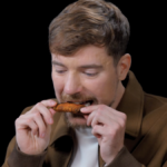 Um homem está sentado em um quarto escuro mordendo uma asa de frango.