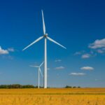 Two wind turbines stand against with a blue sky with cumulus clouds.