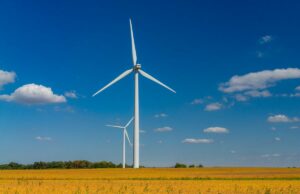 O novo acordo de energia limpa de 1,9 GW do Google inclui uma enorme bateria de 100 horas Two wind turbines stand against with a blue sky with cumulus clouds.