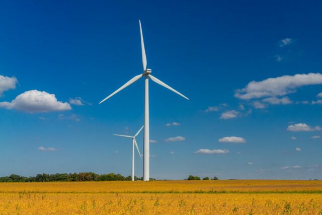 O novo acordo de energia limpa de 1,9 GW do Two wind turbines stand against with a blue sky with cumulus clouds.