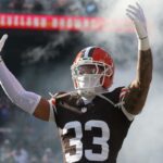 Uma colagem de imagens contendo 1 imagem, a imagem 1 mostra o segurança do Cleveland Browns, Ronnie Hickman (33), levantando os braços com fumaça ao seu redor durante as apresentações dos jogadores