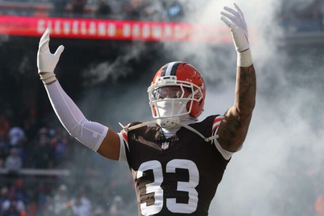 Uma colagem de imagens contendo 1 imagem, a imagem 1 mostra o segurança do Cleveland Browns, Ronnie Hickman (33), levantando os braços com fumaça ao seu redor durante as apresentações dos jogadores