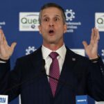 O técnico do New York Giants, John Harbaugh, falando em entrevista coletiva, com os braços levantados e a boca aberta.