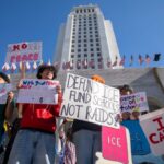 Estudantes protestam contra o ICE em frente à Prefeitura, segurando cartazes que dizem