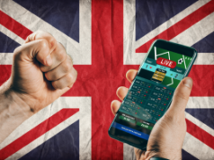 Os requisitos de apostas da Comissão de Jogos do Reino Unido traçam um rumo para 2026 Os requisitos de apostas da Comissão de Jogos do Reino Unido traçam um rumo para 2026. Mão segurando um smartphone exibindo probabilidades de apostas esportivas ao vivo contra um fundo Union Jack, simbolizando jogos de azar online no Reino Unido e mudanças regulatórias.