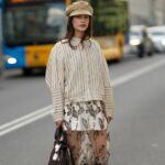 PARIS, FRANÇA - 25 DE JANEIRO: Constance Jablonski usa longos cabelos loiros ondulados com uma parte central, brincos de argola de metal, uma bolsa clutch de couro preta, uma jaqueta preta grande com listras jacquard com logotipo PATOU tonal, gola de couro texturizada e detalhes de fivela de metal em camadas sobre um top preto, uma minissaia combinando, bota skinny de couro preto brilhante, fora de Patou, durante a Paris Fashion Week - Moda masculina outono / inverno 2026-2027, em 25 de janeiro de 2026 em Paris, França (Foto de Edward Berthelot/Getty Images)