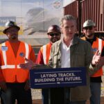 O governador da Califórnia, Gavin Newsom, aperta a mão de um trabalhador do Iron Workers Local 155 enquanto Ian Choudri, CEO da Autoridade Ferroviária de Alta Velocidade da Califórnia, observa.