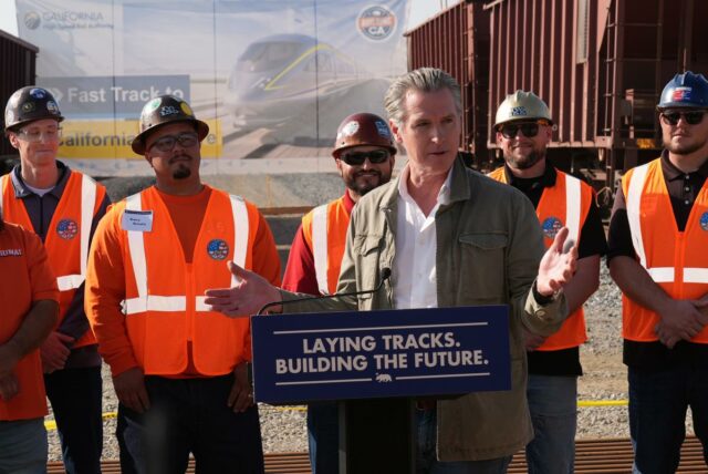O governador da Califórnia, Gavin Newsom, aperta a mão de um trabalhador do Iron Workers Local 155 enquanto Ian Choudri, CEO da Autoridade Ferroviária de Alta Velocidade da Califórnia, observa.