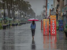 Por que a Califórnia deveria armazenar água e não entrar em pânico com o clima Um homem vestindo um poncho azul e um boné de beisebol anda de skate em um calçadão molhado, com palmeiras e edifícios ao fundo durante fortes chuvas.