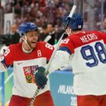 Os jogadores dinamarqueses de hóquei no gelo Lars Eller, Oliver Bjorkstrand e Nikolaj Ehlers em uniformes vermelhos e brancos durante uma partida nos Jogos Olímpicos de Inverno de Milão Cortina 2026.
