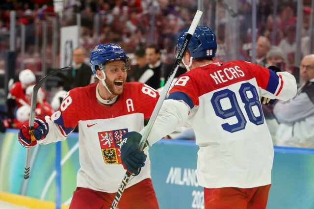 Os jogadores dinamarqueses de hóquei no gelo Lars Eller, Oliver Bjorkstrand e Nikolaj Ehlers em uniformes vermelhos e brancos durante uma partida nos Jogos Olímpicos de Inverno de Milão Cortina 2026.