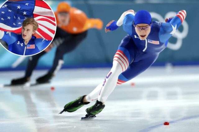 Jordan Stolz, da equipe de patinação de velocidade dos Estados Unidos, vestindo um terno azul, branco e vermelho com outro patinador de velocidade desfocado ao fundo durante a prova masculina de 500m.