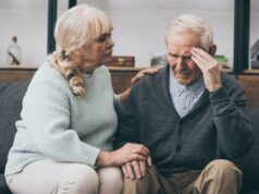 Querida Abby: Estou casada há 50 anos – e meu marido nunca se desculpou por seu caso Uma mulher mais velha, de cabelos loiros, está sentada na cama, segurando a testa com dor de cabeça.