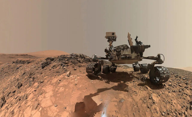 Rover da NASA em Marte encontra novas pistas apontando para O rover Curiosity Mars da NASA é visto no local de onde desceu para perfurar um alvo rochoso chamado 'Buckskin' na parte inferior do Monte Sharp neste autorretrato de baixo ângulo tirado em 5 de agosto de 2015 e divulgado em 19 de agosto de 2015. A selfie combina várias imagens componentes tiradas pelo Mars Hand Lens Imager (MAHLI) da Curiosity.