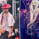 Shia LaBeouf, parecendo embriagado, vestido com um chapéu vermelho e branco com livro falso e acabamento fofo, camiseta branca, colete vermelho e bege e calça escura, segurando uma garrafa de cerveja.