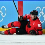 O jogador de hóquei no gelo Sidney Crosby com uma camisa vermelha com o número 87, deitado no gelo após uma lesão.