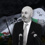 Thomas Goldstein condenado em um amplo caso fiscal federal: pôquer de apostas altas e a queda de um advogado da Suprema Corte. Thomas Goldstein, de terno e gravata, fala em dois microfones, em um cenário gráfico de cartas de baralho enormes, incluindo damas de paus e ouros, sugerindo um tema relacionado a jogos de azar ou pôquer.