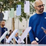 Tim Cook não descartou aumentos de preços dos produtos Apple, e este é o motivo | A foto mostra funcionários conversando atrás de uma tela de iPhones em uma loja da Apple