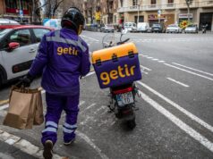 Uber comprará braço de entrega da turca Getir Getir delivery driver holding grocery bags and walking to Getir delivery bike