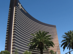 Wynn Resorts enfrenta crescentes consequências legais após a expansão de ações judiciais de ataques cibernéticos em todo o país Wynn Resorts enfrenta crescentes consequências legais depois que os processos de ataques cibernéticos se expandem em todo o país. Vista externa da torre curva do hotel Wynn Las Vegas em vidro bronze com o logotipo Wynn no topo, emoldurada por palmeiras contra um céu azul claro.