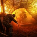 Uma mulher visita o memorial coberto de neve aos combatentes ucranianos e estrangeiros caídos na Praça da Independência, em Kiev, em 13 de janeiro de 2026, em meio à invasão russa da Ucrânia. (Foto de Sergei GAPON/AFP)