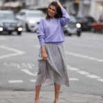 Diane Batoukina usa vestido midi de seda branca com estampa de listras azuis e marinho, mangas curtas e gola pontuda da Sandro. Um lenço de seda Sandro combinando está amarrado frouxamente no decote. Uma mini bolsa branca com alça de corrente e detalhes dourados da Chanel é usada na transversal. O calçado consiste em sandálias brancas de salto aberto da Aeyde. Os óculos de sol quadrados Dior com lentes gradientes escuras completam o visual. Cabelo castanho longo e liso é penteado com uma parte central. Os lábios ficam sutilmente coloridos e a pele parece lisa e uniforme. Foto de corpo inteiro, durante uma sessão de fotos de moda de rua, em 28 de abril de 2025 em Paris, França.