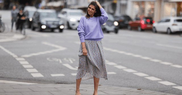 Diane Batoukina usa vestido midi de seda branca com estampa de listras azuis e marinho, mangas curtas e gola pontuda da Sandro. Um lenço de seda Sandro combinando está amarrado frouxamente no decote. Uma mini bolsa branca com alça de corrente e detalhes dourados da Chanel é usada na transversal. O calçado consiste em sandálias brancas de salto aberto da Aeyde. Os óculos de sol quadrados Dior com lentes gradientes escuras completam o visual. Cabelo castanho longo e liso é penteado com uma parte central. Os lábios ficam sutilmente coloridos e a pele parece lisa e uniforme. Foto de corpo inteiro, durante uma sessão de fotos de moda de rua, em 28 de abril de 2025 em Paris, França.