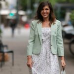 Alexandra Pereira usa óculos escuros brancos, brincos prateados e strass, vestido midi de couro azul claro brilhante com decote em V / sem mangas / cinto / fenda, bolsa rosa claro da Salvatore Ferragamo, sapatos de salto bloco de couro branco com nó bordado na biqueira, anéis, fora do desfile da Ferragamo durante a Milan Fashion Week - Primavera / Verão 2022 em 25 de setembro de 2021 em Milão, Itália.