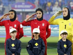 3 jogadores de futebol iranianos que receberam asilo da Austrália estão voltando para casa – à medida que aumentam os temores sobre sua segurança Três jogadoras de futebol iranianas fazem continência com três crianças na frente delas, enquanto chove.