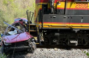 5 mortos após trem de carga atingir van em cruzamento ferroviário na zona rural do Mississippi Uma van vermelha gravemente danificada ao lado de um trem de carga nos trilhos.