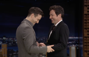 A estrela de Bridgerton, Luke Thompson, ensina a Jimmy Fallon uma dança elegante do show Dois homens ficam de frente um para o outro, rindo.