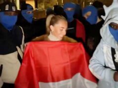 A estrela pornô Bonnie Blue é acusada de imitar ato sexual fora da embaixada da Indonésia no Reino Unido Bonnie Blue (Tia Billinger) sorrindo em frente à Embaixada da Indonésia no Reino Unido, cercada por pessoas com balaclavas azuis e segurando a bandeira da Indonésia.