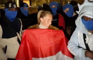 A estrela pornô Bonnie Blue é acusada de imitar ato sexual fora da embaixada da Indonésia no Reino Unido Bonnie Blue (Tia Billinger) sorrindo em frente à Embaixada da Indonésia no Reino Unido, cercada por pessoas com balaclavas azuis e segurando a bandeira da Indonésia.