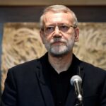 Ali Larijani, conselheiro sênior do Líder Supremo do Irã, falando em um pódio com um microfone.