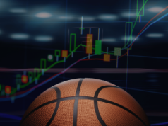 Anúncios de previsão do mercado aumentam à medida que as apostas do March Madness atingem níveis recordes Anúncios de previsão do mercado aumentam à medida que as apostas no March Madness atingem níveis recordes. Uma bola de basquete em primeiro plano com um gráfico financeiro brilhante ao fundo mostrando castiçais crescentes e linhas de tendência ascendentes, simbolizando o crescimento dos mercados de apostas esportivas em torno de eventos de basquete.