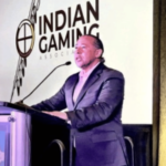 Presidente da Indian Gaming Association falando no pódio durante conferência sobre política de jogos tribais e regulamentação de apostas esportivas. IGA apóia projeto bipartidário do Senado visando mercados de previsão esportiva