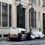 Policiais franceses e vans estacionadas em frente a um prédio.