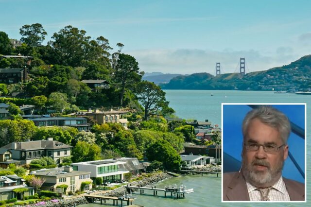 O autor americano Brian Doherty de terno e gravata, falando com a mão levantada.