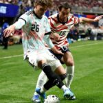 Weston McKennie (8), dos Estados Unidos, marca contra o goleiro belga Senne Lammens durante o primeiro tempo de um amistoso internacional de futebol, sábado, 28 de março de 2026, em Atlanta. (Foto AP/Mike Stewart)