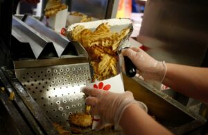 Chick-fil-A muda a receita para batatas fritas com waffle após reação dos fãs Um funcionário usando luvas transparentes prepara batatas fritas com waffles em um recipiente de papel branco em um restaurante Chick-fil-A.