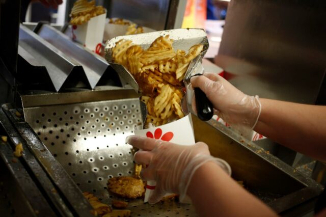 Um funcionário usando luvas transparentes prepara batatas fritas com waffles em um recipiente de papel branco em um restaurante Chick-fil-A.
