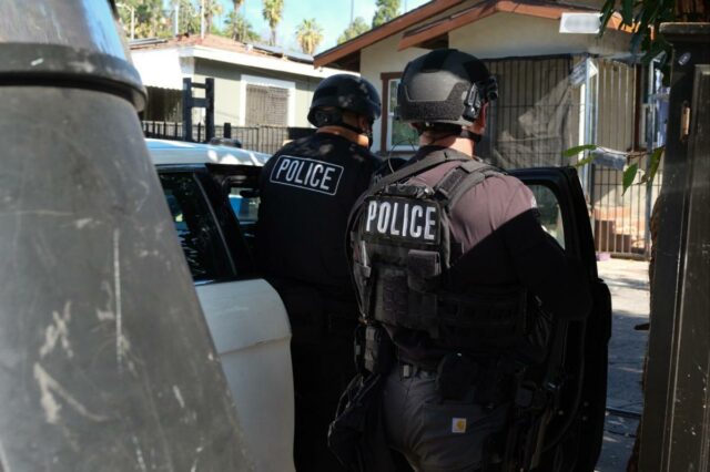 Coloque algemas em gangsters, não em policiais Um policial por trás passa por placas de caixas eletrônicos e placas anunciando serviços de transferência de dinheiro.