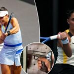 Uma tenista com roupa azul clara e viseira bate em uma bola de tênis com uma raquete.